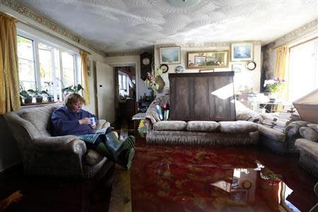 Sally Vize, 61, has a cup of tea and reads a magazine in the flooded living room of her house in the Somerset village of Moorland February 13, 2014. British ministers will meet representatives of the insurance industry on Tuesday, February 18, who will brief them on their progress in dealing with victims of winter floods across southern England. REUTERS/Cathal McNaughton