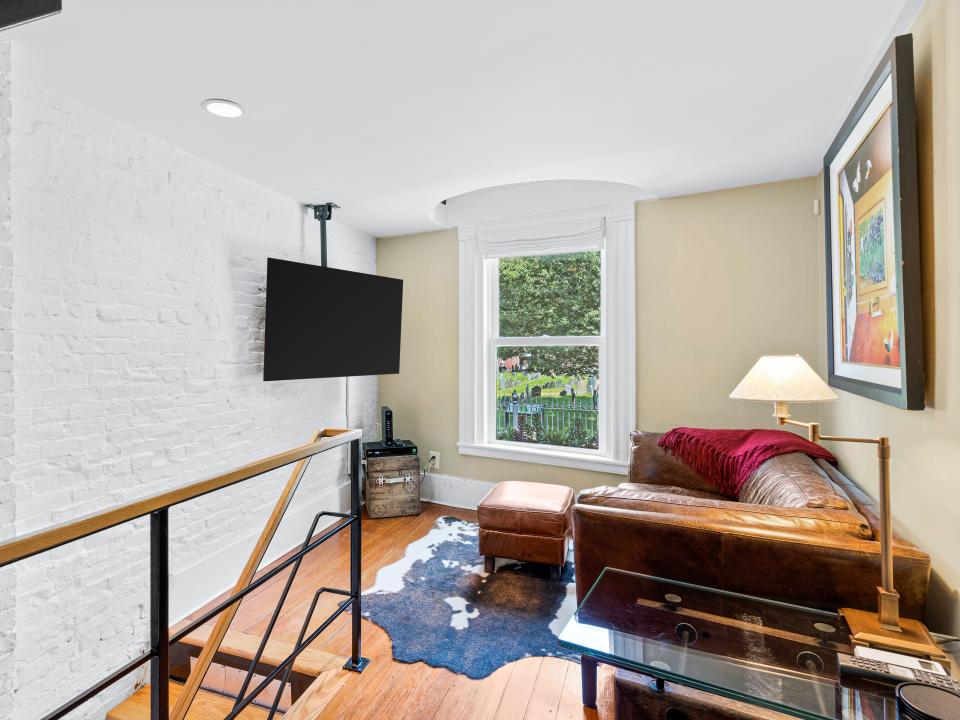 Stairs lead to a living room with wood floors and a mounted TV on the left side. There's a window in the back