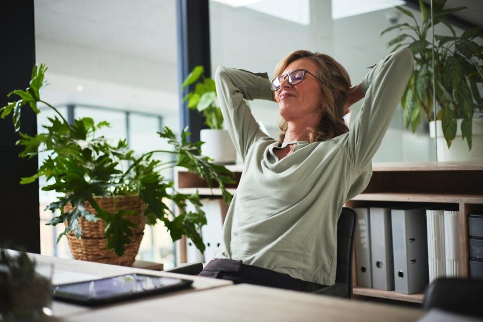 A person sitting at a desk smiles while leaning back in a chair and closing their eyes.