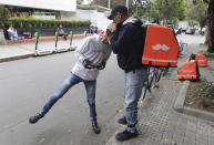 Venezuelan bicycle courier Luis Tarre, 60, kisses the head of his 20-year-old son Raul as they wait for Rappi delivery orders in Bogota, Colombia, Wednesday, July 17, 2019. Critics of the app say that a large number of couriers have basically become full-time workers, and lawmakers in Colombia and Argentina are considering regulations to boost protection for the workers. (AP Photo/Fernando Vergara)