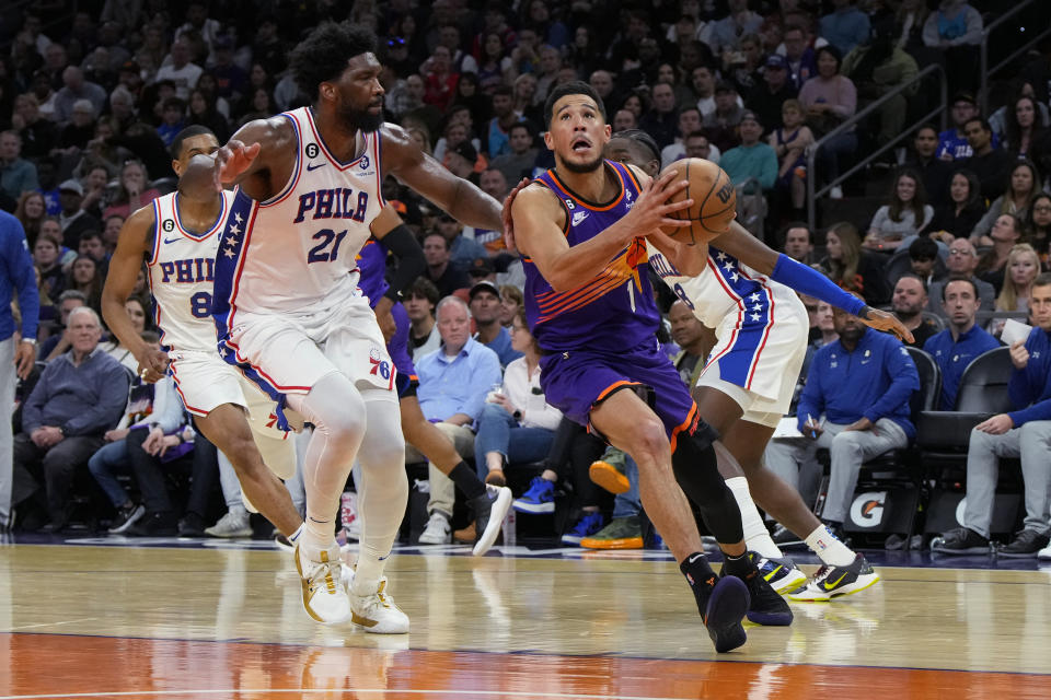 Phoenix Suns guard Devin Booker (1) drives past Philadelphia 76ers center Joel Embiid (21) during the second half of an NBA basketball game Saturday, March 25, 2023, in Phoenix. The Suns won 125-105. (AP Photo/Rick Scuteri)