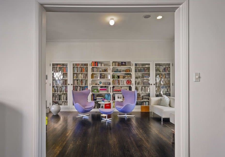 A view of a library shows white shelves filled with books with two Modernist chairs in lavender.