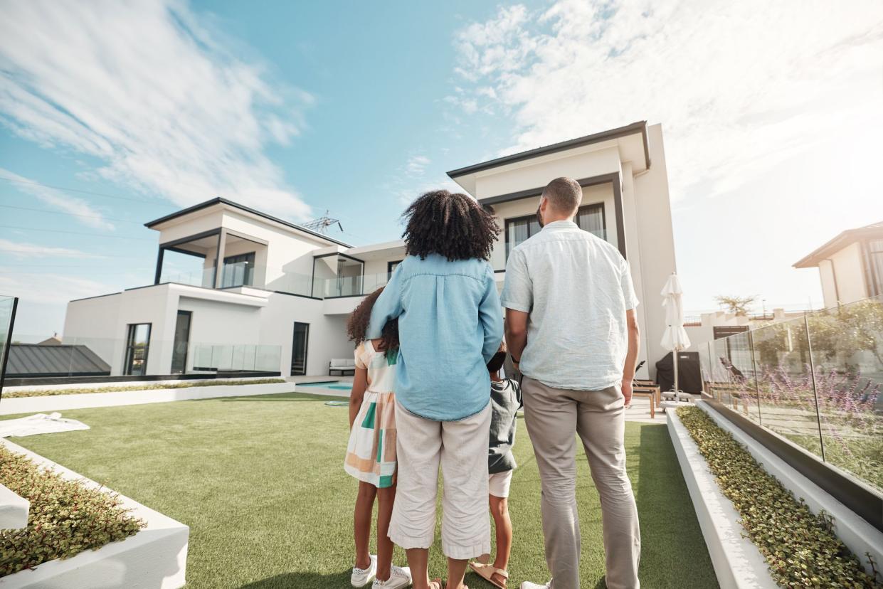 Backs of Couple With Two Kids in Front Yard Looking at Their New Home