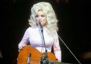 <p>From the start, Parton's style always featured some sort of sparkle, seen here in an embellished high-neck, baby pink look on stage in 1976. </p>