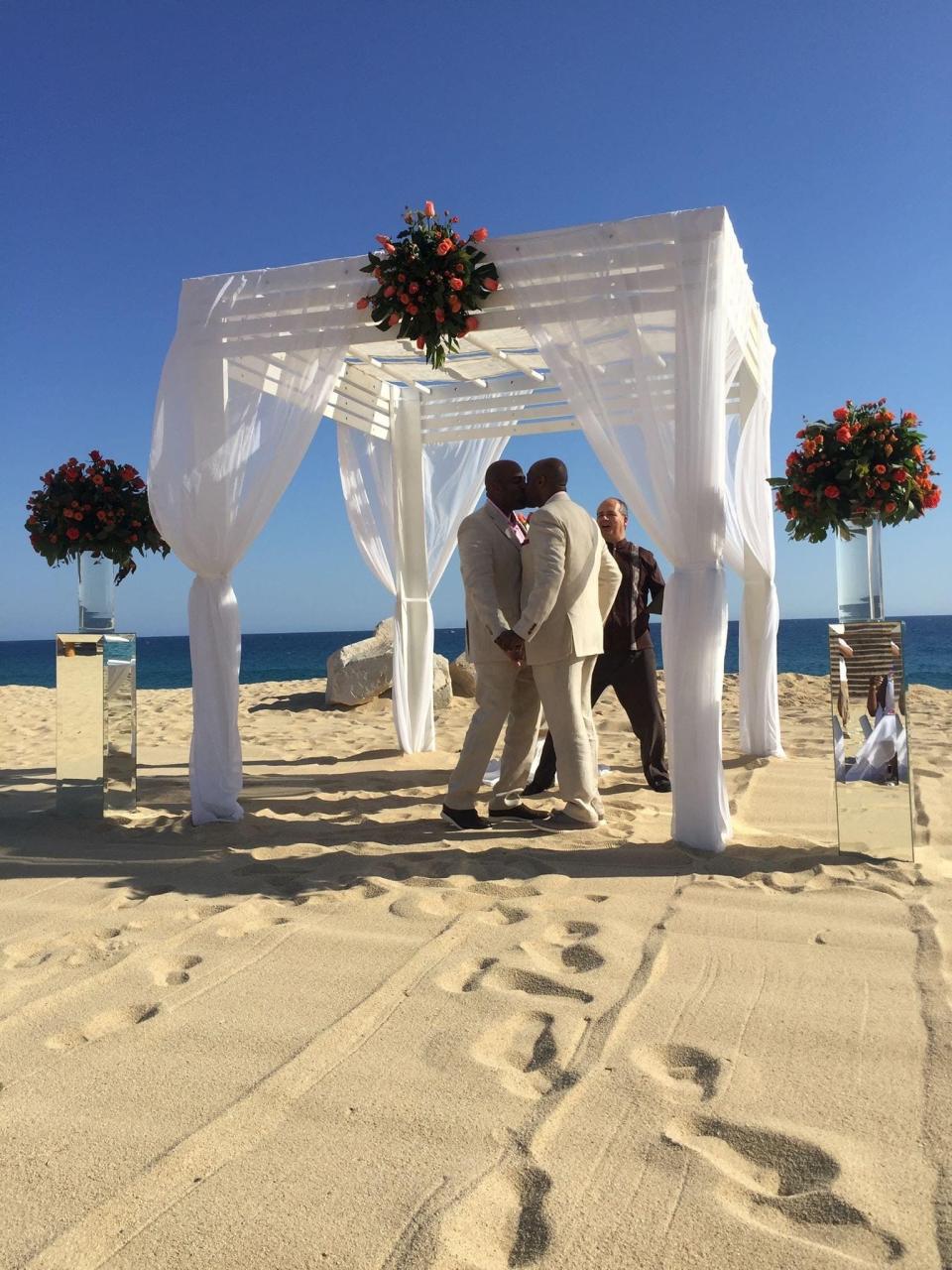 couple kissing under a pergola on the beach getting married