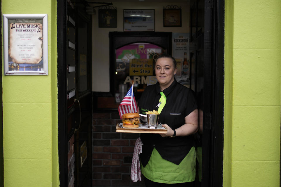 Sarah Delahunt holds out a tray with a burger and fries adorned with a United States flag in Carlingford, Ireland, Tuesday, April 11, 2023, as final preparations are made for the visit of President Joe Biden to the town later in the week. President Biden is visiting Northern Ireland and Ireland to celebrate the 25th Anniversary of the Good Friday Agreement. (AP Photo/Christophe Ena)