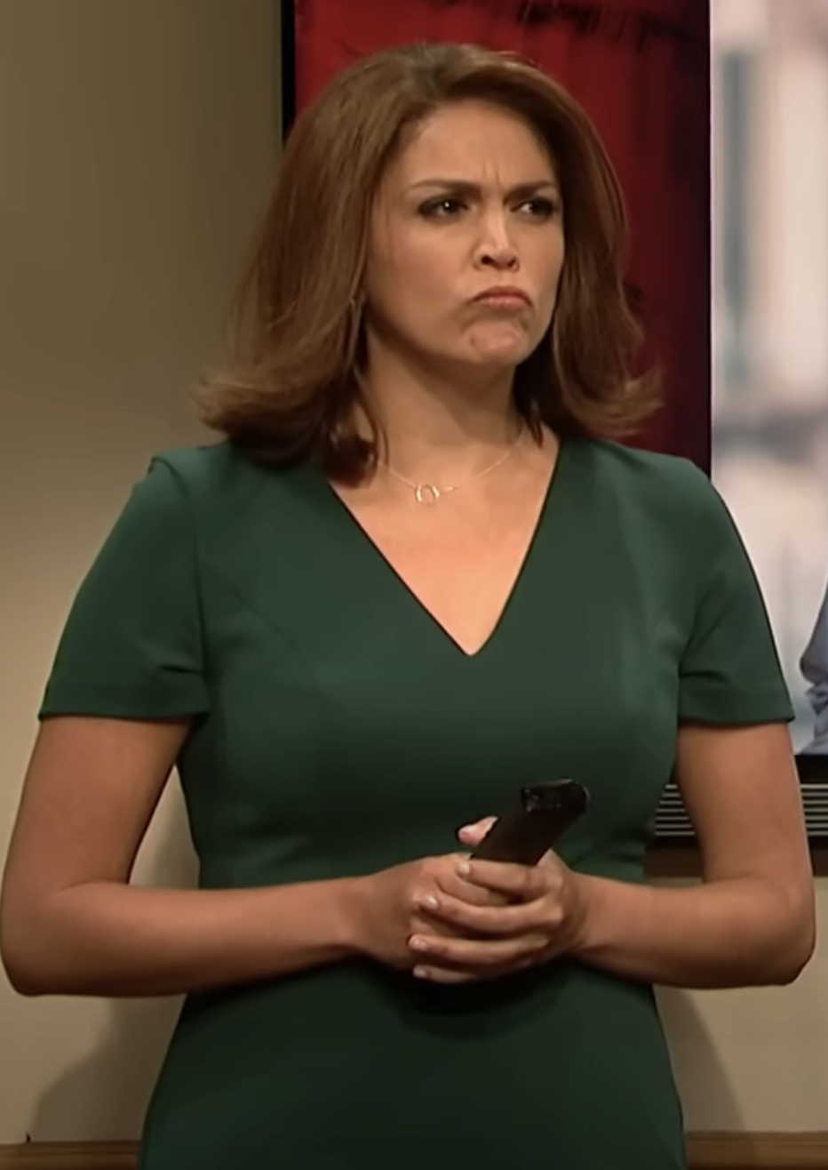 Cecily Strong as an admissions counselor standing indoors, holding a remote control, making a face