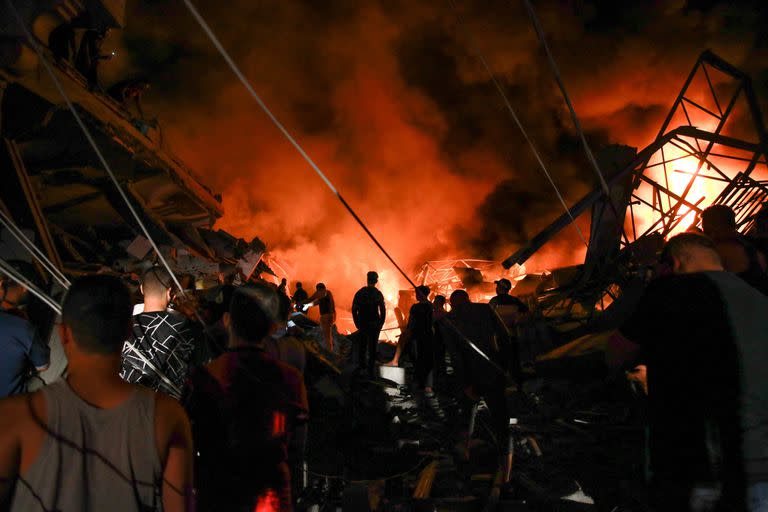 El humo y el fuego se elevan desde los edificios mientras la gente se reúne en medio de la destrucción tras un ataque israelí en la ciudad de Gaza.