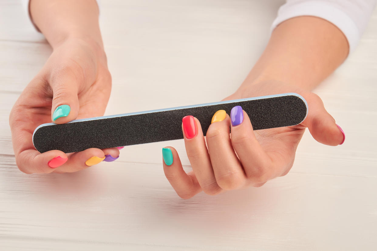 woman using nail file on colored nails