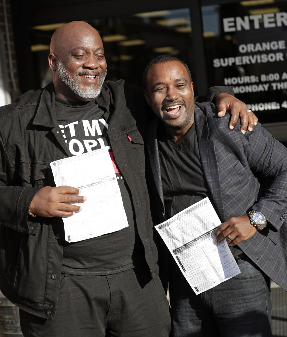 FILE- In this Jan. 8, 2019, file photo, Desmond Meade, president of the Florida Rights Restoration Coalition, left, and David Ayala, husband of State Attorney Aramis Ayala, celebrate after registering to vote at the Supervisor of Elections in Orlando, Fla. Both had been convicted of felonies. The effort to register Florida’s newly eligible felons to vote is being stymied by the coronavirus pandemic and a disputed requirement that felons pay a series of costs. (AP Photo/John Raoux, File)