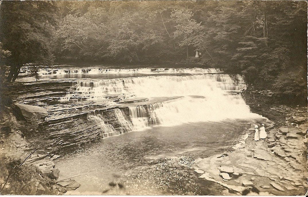 Two women, dressed in Victorian-era white, look at the waterfall at the present site of the Gorge Dam on the Cuyahoga River. It remains to be seen what geologic features will be revealed when the dam removal project is completed in 2026.