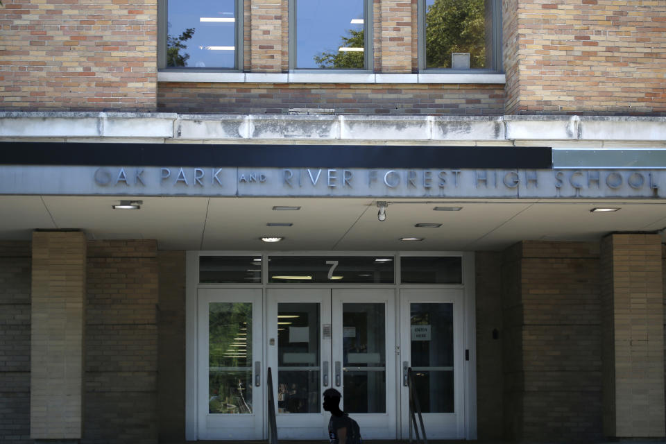 A student walks past Oak Park and River Forest High School on Wednesday, Aug. 17, 2022, in Oak Park, Ill. Security experts say that keeping perimeter doors locked during class time is key to keeping students safe. They also concede that, even with stringent security, keeping guns out of the nation's schools is difficult. (AP Photo/Martha Irvine)