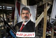 FILE PHOTO: A poster of Egypt's President Mursi is seen near members of Muslim Brotherhood after night clashes with anti-Mursi in Giza