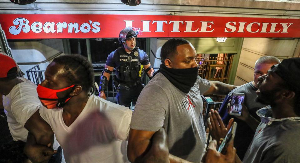 Five men, including Christopher Gales, Darren Lee Jr, Ricky McClellan and Julian "New Heightz" De La Cruz linked arms to keep a crowd of protesters away from LMPD officer Galen Hinshaw on the first night of protests in Louisville on May 28, 2020.