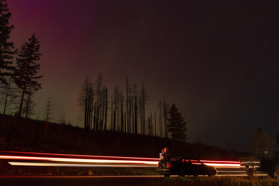 In this image taken with a long exposure, cars pass by as people look at the night sky towards the northern lights, or Aurora Borealis, on Friday, May 10, 2024, in Estacada, Ore. Brilliant purple, green, yellow and pink hues of the Northern Lights were reported worldwide, with sightings in Germany, Switzerland, London, and the United States and Canada. (AP Photo/Jenny Kane)