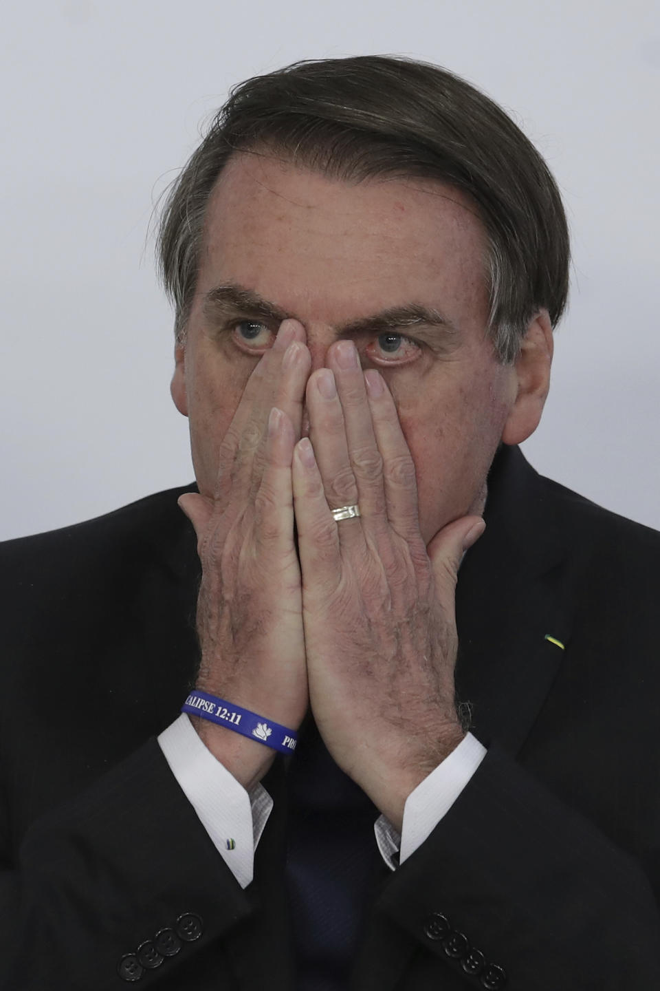 Brazil's President Jair Bolsonaro covers his face during ceremony at the Planalto Presidential Palace in Brasilia, Brazil, Monday, March 25, 2019. Brazil's president says he is "open to dialogue" about an ambitious pension reform that has become a central pillar of his administration's agenda. (AP Photo/Eraldo Peres)