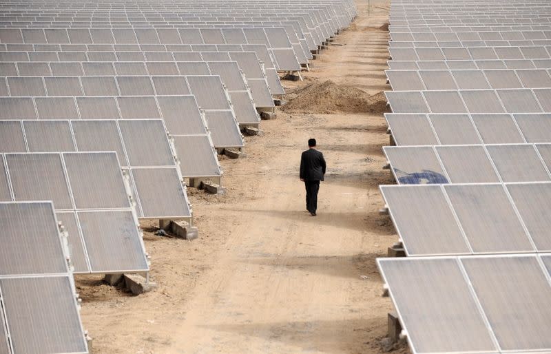 FILE PHOTO: A man walks through solar panels at a solar power plant under construction in Aksu