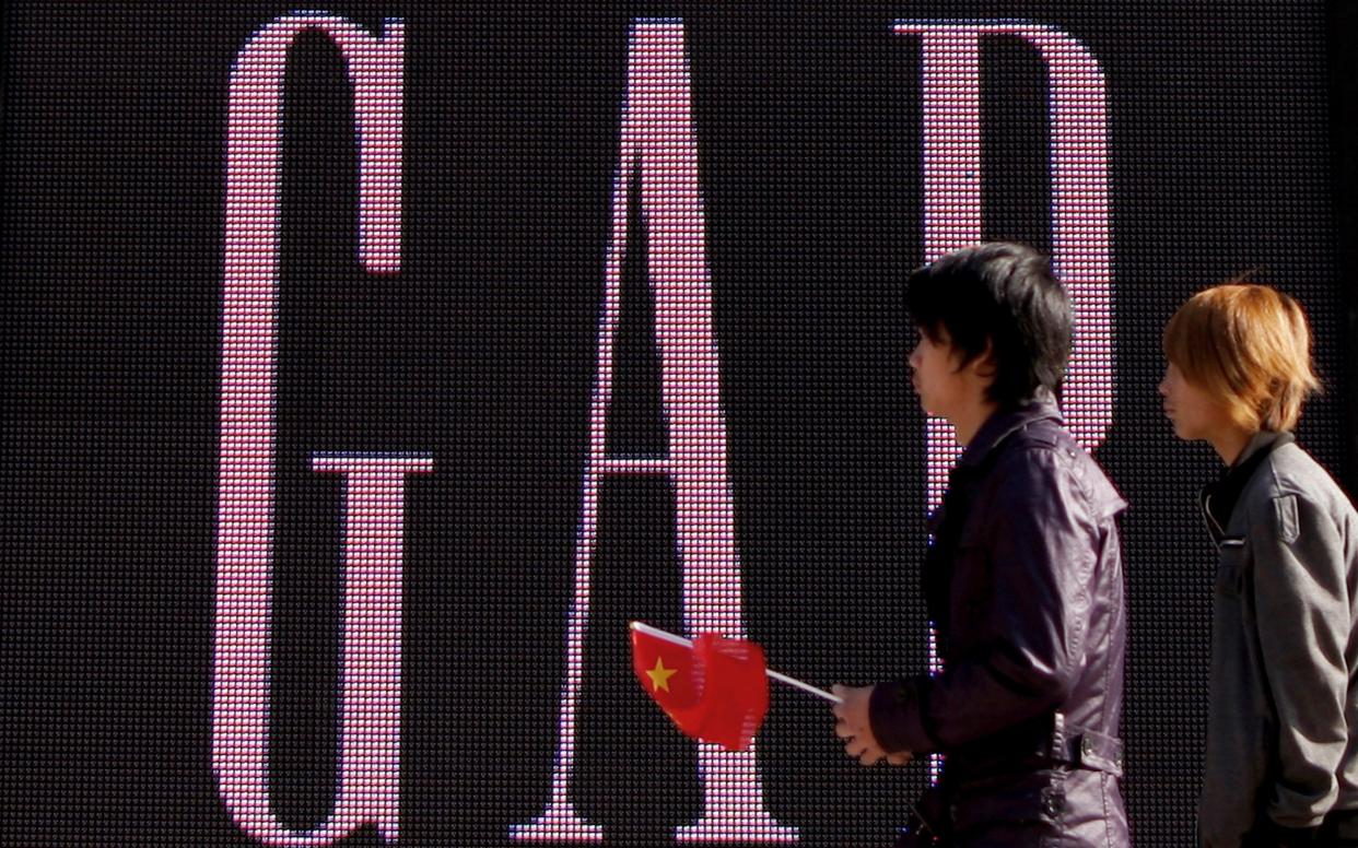 A man carries a Chinese flag as he walks past a GAP store in Beijing - AP