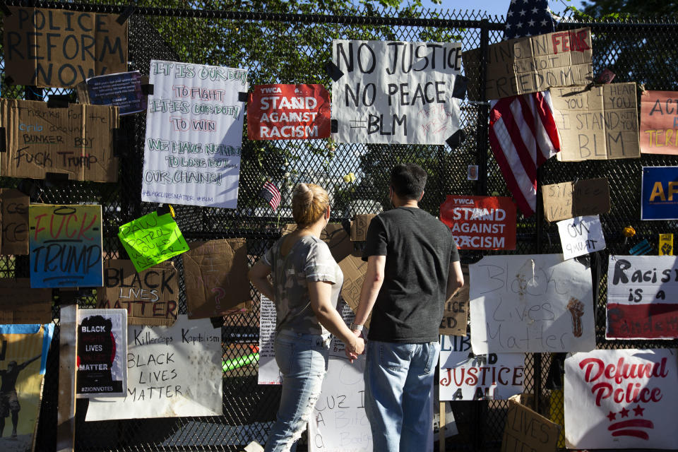 A couple reads signs left on a fence at Lafayette Square near the White House, during ongoing protests against police brutality and racism, on June 7, 2020 in Washington, DC. (Jose Luis Magana/AFP via Getty Images)