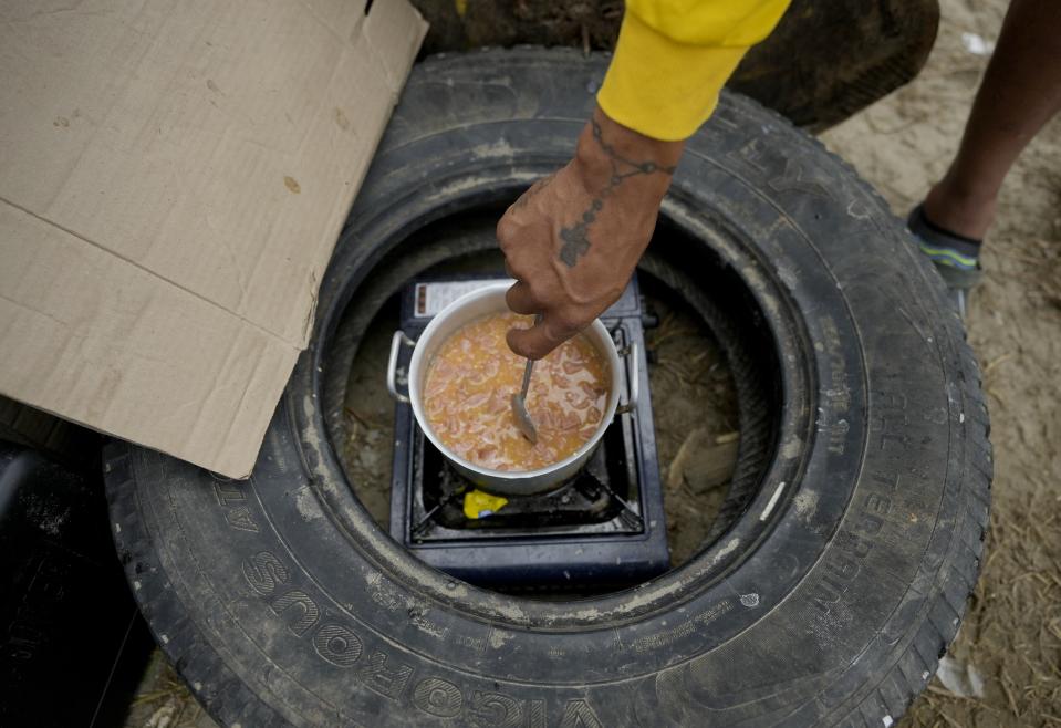 Un venezolano cocina arroz y jamón en una hornilla portátil en Necocli, Colombia, el lugar donde los migrantes toman lanchas para ir hasta Acandi, a las puertas de la selva del Darién, el 13 de octubre de 2022. Algunos venezolanos están reconsiderando su viaje hacia Estados Unidos luego de que la Casa Blanca anunció el 12 de octubre que los venezolanos que crucen la frontera a pie o a nado serán devueltos de inmediato a México sin derecho a solicitar asilo. (AP Foto/Fernando Vergara)