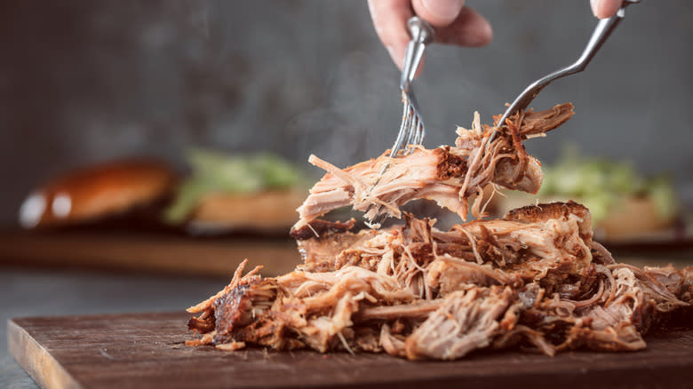 pulled pork being shredded on cutting board