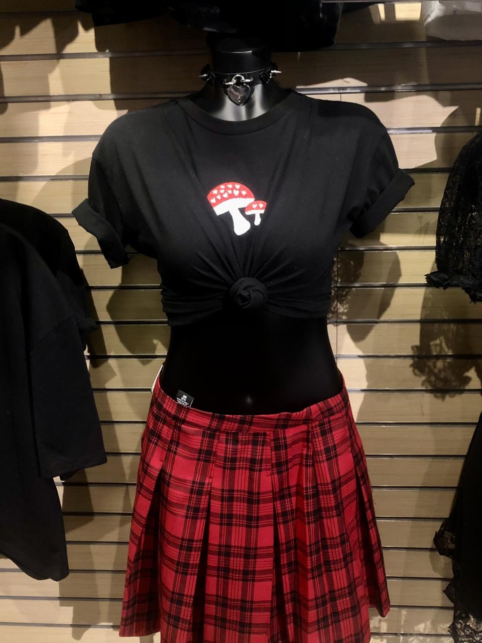 Display model of mushroom shirt tied at the midsection, paired with a red plaid skirt and leather studded choker