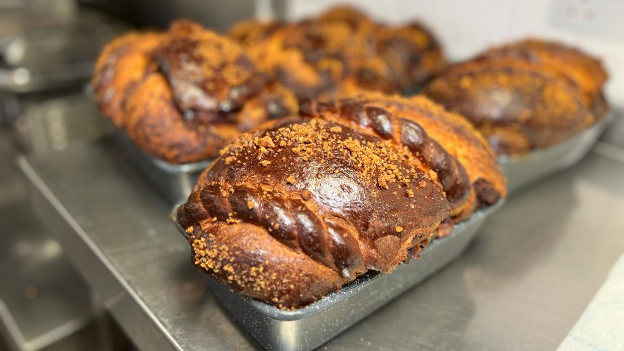 Cozonac bread is in its baking tray on a metal surface after coming out of the oven. It looks crispy and brown with braided decorations on the bread.