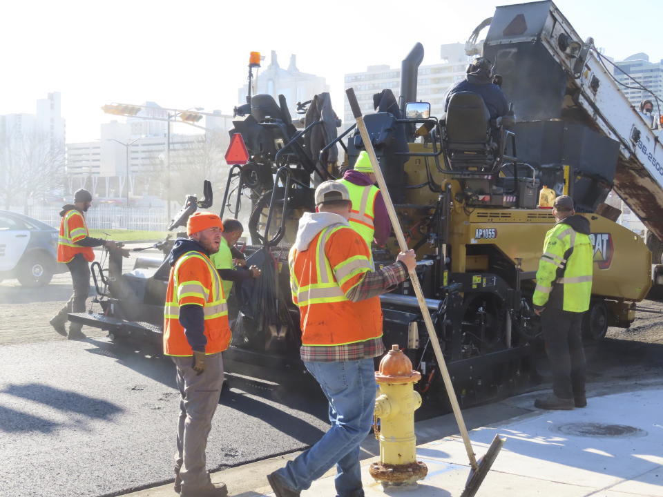 Workers repave a section of Atlantic Avenue in Atlantic City, N.J., on Dec. 13, 2023, as part of a project to reduce the main road through the gambling resort from four lanes to two. Federal and state funds that paid for the $24 million repaving and traffic light synchronization project also require a pedestrian safety component, in this case reducing the size of the roadway. (AP Photo/Wayne Parry)