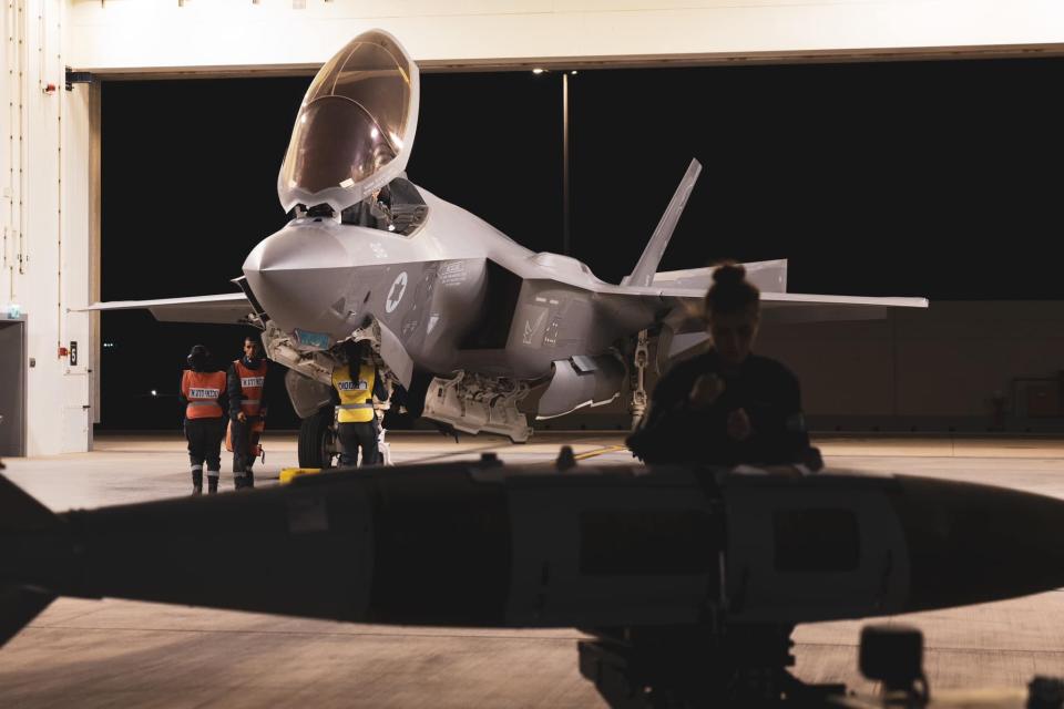 a crew works on a fighter jet with a munition in the foreground