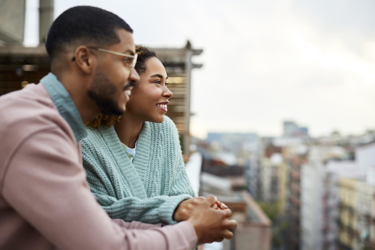 Happy young couple looking away while holding hands at rooftop. Smiling woman is spending leisure time with boyfriend. They are enjoying at building terrace.