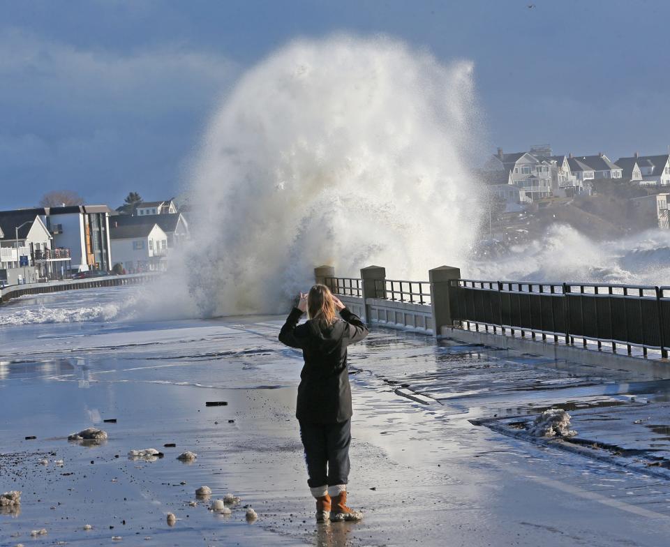 A woman takes photos of waves crashing over the seawall on Ocean Boulevard at Hampton Beach at high tide in the morning Wednesday, Jan. 10, 2024.