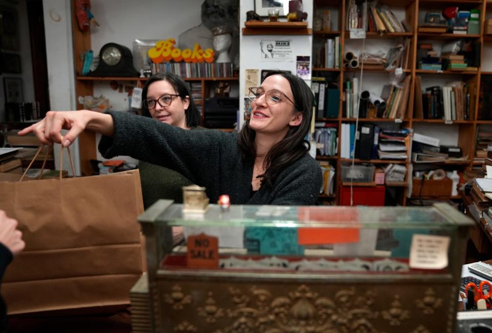 Cellar Stories Books manager Victoria Forsberg-Lary hands a purchase to a customer after ringing the sale on the book store's vintage cash register. Behind her is co-manager Justine Johnson. The story is closing after many years in Downtown Providence.