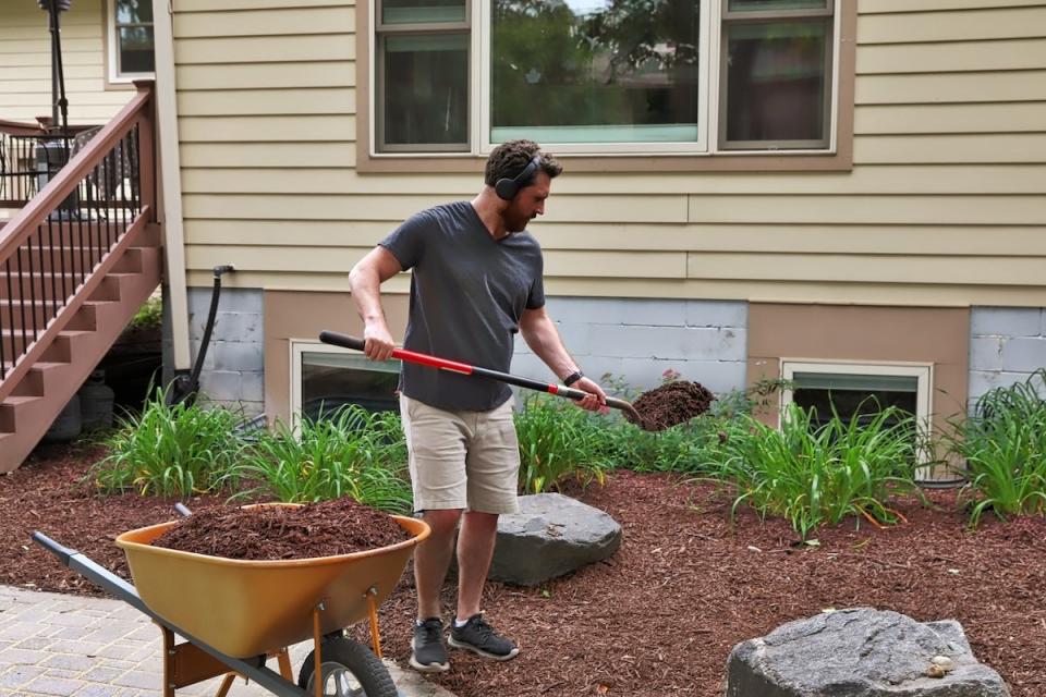 A homeowner laying down wood mulch in his backyard flower beds.