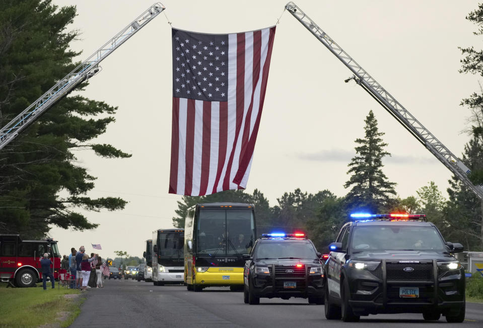 A procession of vehicles from the Fargo Police Department pass beneath an American Flag draped by fire trucks over Patriot Avenue as they escort fallen Officer Jake Wallin and his family from Fargo to Pequot Lakes High School for a memorial service Saturday, July 22, 2023 in Pequot Lakes, Minn. Wallin was killed July 14 when a man armed with 1,800 rounds of ammunition, multiple guns and explosives began firing on officers who were responding to a traffic crash.(Anthony Souffle/Star Tribune via AP)