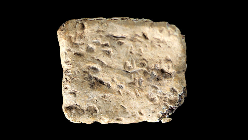 Curse tablet made of light colored stone in the shape of a rough square.