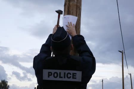 A French policeman posts the official document that announces the dismantling of the makeshift camp called the "Jungle", in Calais, France, October 21, 2016. REUTERS/Pascal Rossignol