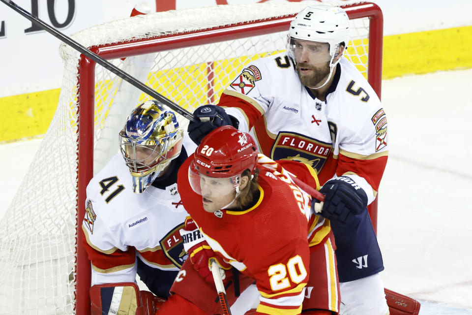Calgary Flames Blake Coleman, center, is pushed away by Florida Panthers Arron Ekblad, right, beside Florida goalie Anthony Stolarz during the first period of an NHL hockey game in Calgary, Alberta., Monday, Dec. 18, 2023. (Larry MacDougal/The Canadian Press via AP)