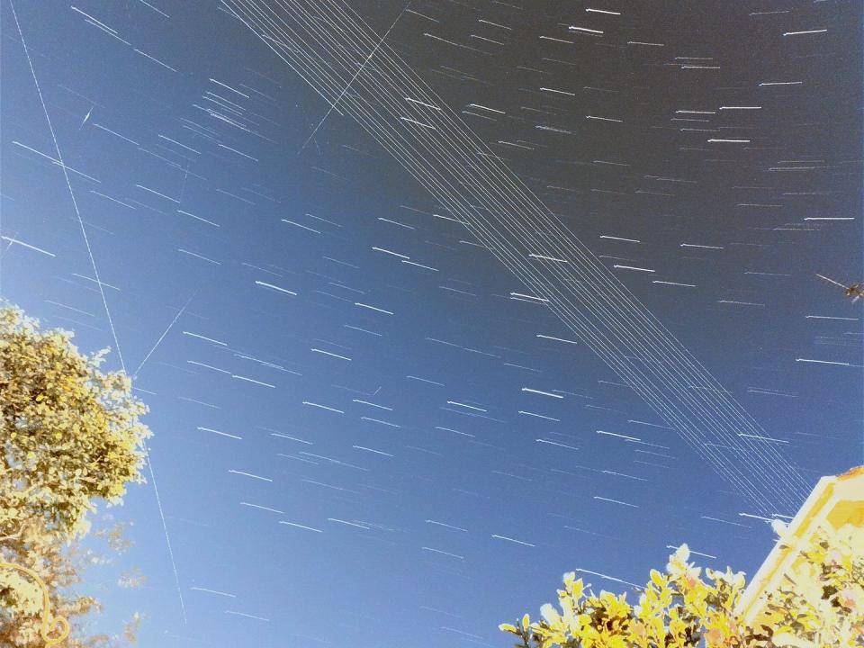 A photo of the night sky showing telegraph wires, trees and streaks of light