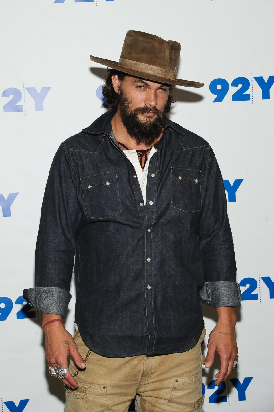 Jason Momoa wears a wide-brimmed hat, dark denim shirt, and beige pants at a 92Y event