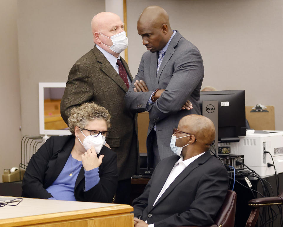 Defense attorney Kobby Warren, standing, right, listens to attorney Mark Watson, top left, as his client Billy Chemirmir, seated right, waits for motions and language being sent to the jury in his capital murder trial at the Frank Crowley Courts Building in Dallas, Friday, Nov. 19, 2021. He was joined by private investigator Tonia Silva seated, left. Chemirmir, 48, faces life in prison without parole if convicted of capital murder for smothering Lu Thi Harris, 81, and stealing her jewelry. He is accused of killing at least 18 women in Dallas and Collin counties. (Tom Fox/The Dallas Morning News via AP, Pool)