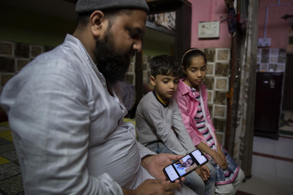 Haroon, holds a mobile phone as his nephew and niece look at the photograph of their father who was shot and killed by their Hindu neighbors during February 2020 communal riots, in North Ghonda, one of the worst riot affected neighborhood, in New Delhi, India, Friday, Feb. 19, 2021. As the first anniversary of bloody communal riots that convulsed the Indian capital approaches, Muslim victims are still shaken and struggling to make sense of their struggle to seek justice. (AP Photo/Altaf Qadri)