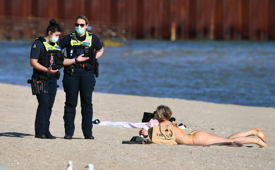 Police speak to a woman enjoying the unusually warm spring weather at St Kilda Beach in Melbourne earlier this month. Source: Getty