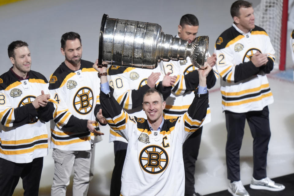 Former Boston Bruins defenseman Zdeno Chara, center, holds the Stanley Cup trophy above his head as he introduced with other former Bruins players during a Return of a Champion ceremony before an NHL hockey game between the Toronto Maple Leafs and the Bruins, Thursday, March 7, 2024, in Boston. (AP Photo/Steven Senne)