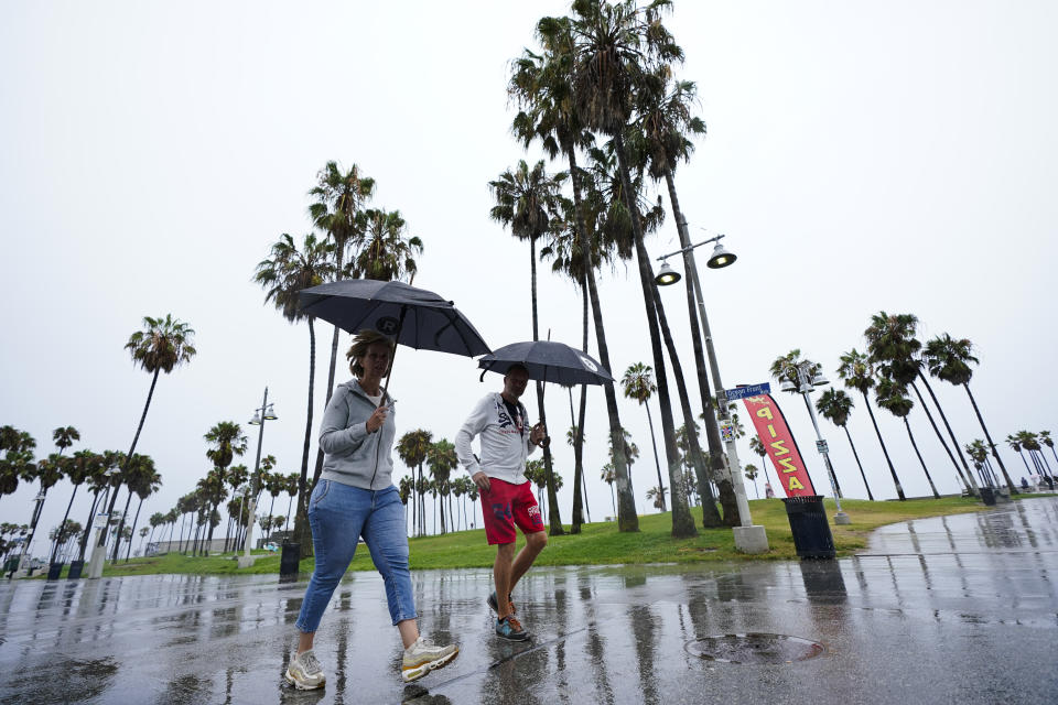 People walk along Venice Beach in the rain, Sunday, Aug. 20, 2023, in Los Angeles. Tropical Storm Hilary swirled northward Sunday just off the coast of Mexico's Baja California peninsula, no longer a hurricane but still carrying so much rain that forecasters said "catastrophic and life-threatening" flooding is likely across a broad region of the southwestern U.S. (AP Photo/Ryan Sun)