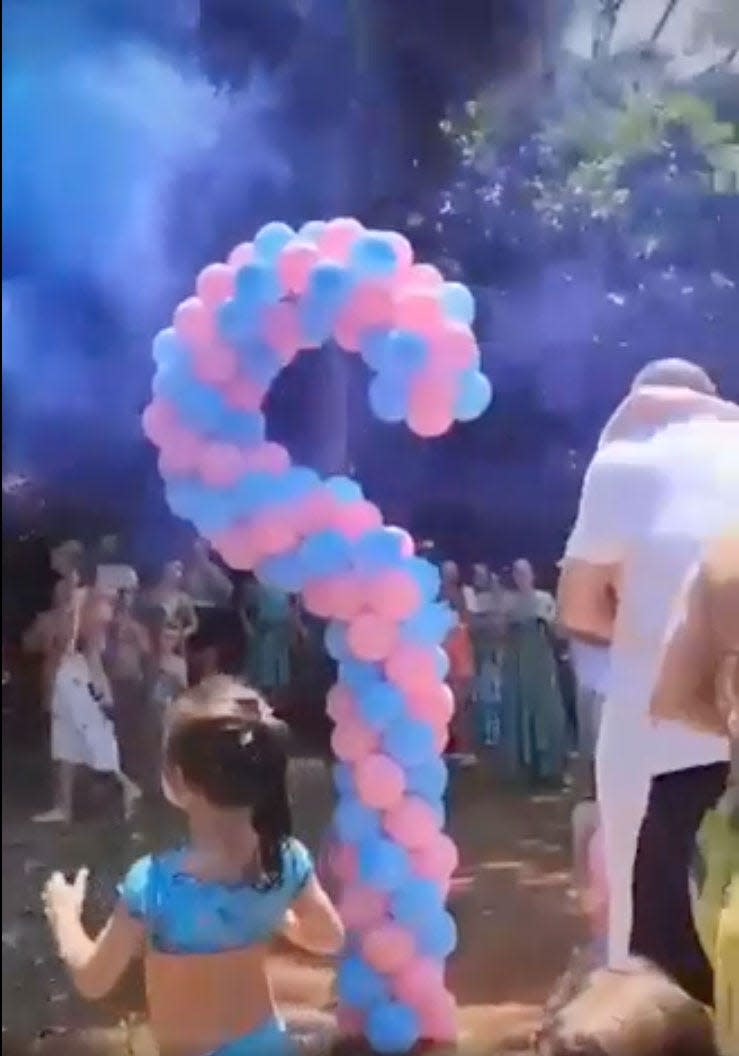 Screenshot of a video uploaded to Reddit showing two people embracing next to a question mark made of blue and pink balloons