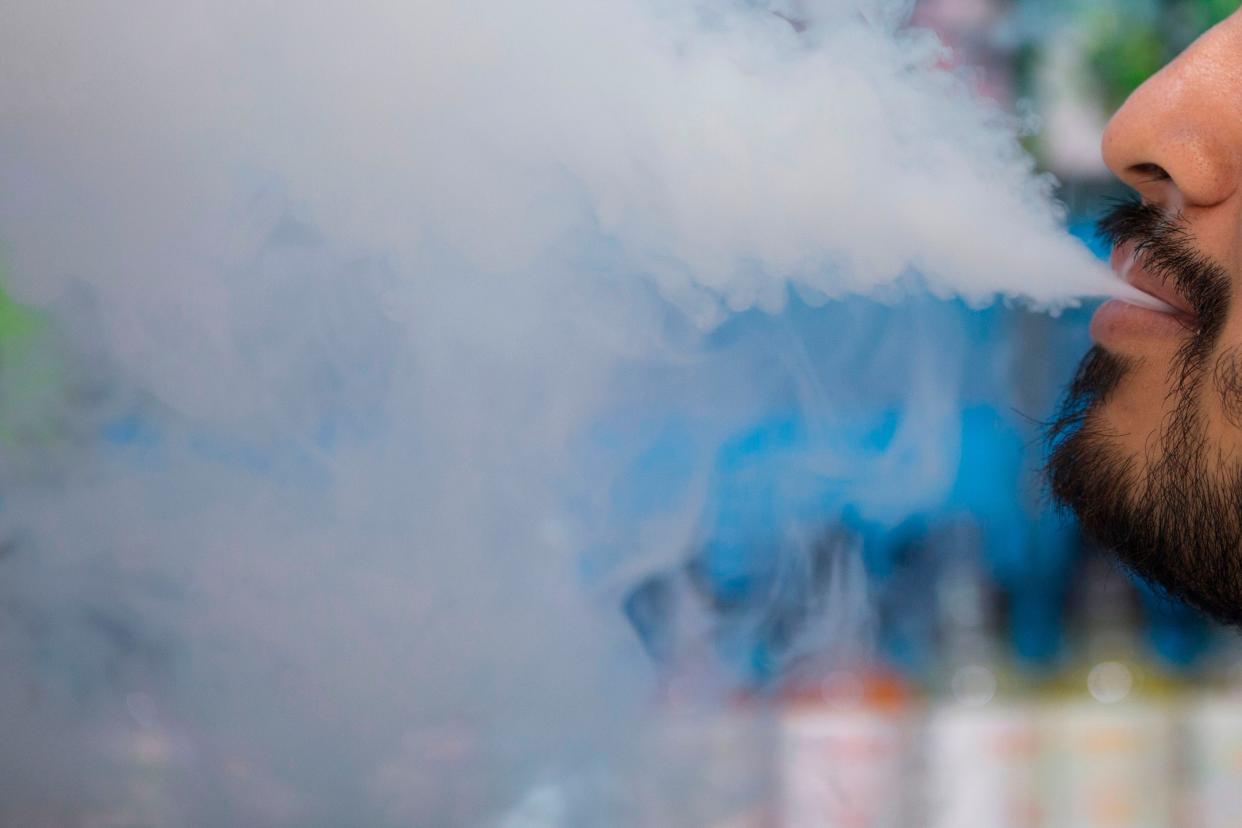 This 2019 file photo shows a man smoking an electronic cigarette inside a vape shop in Washington, D.C. Oregon environmental regulators have fined a vaping liquid manufacturer and distributor $32,700 for multiple hazardous waste violations at its facilities in Eugene and Springfield.