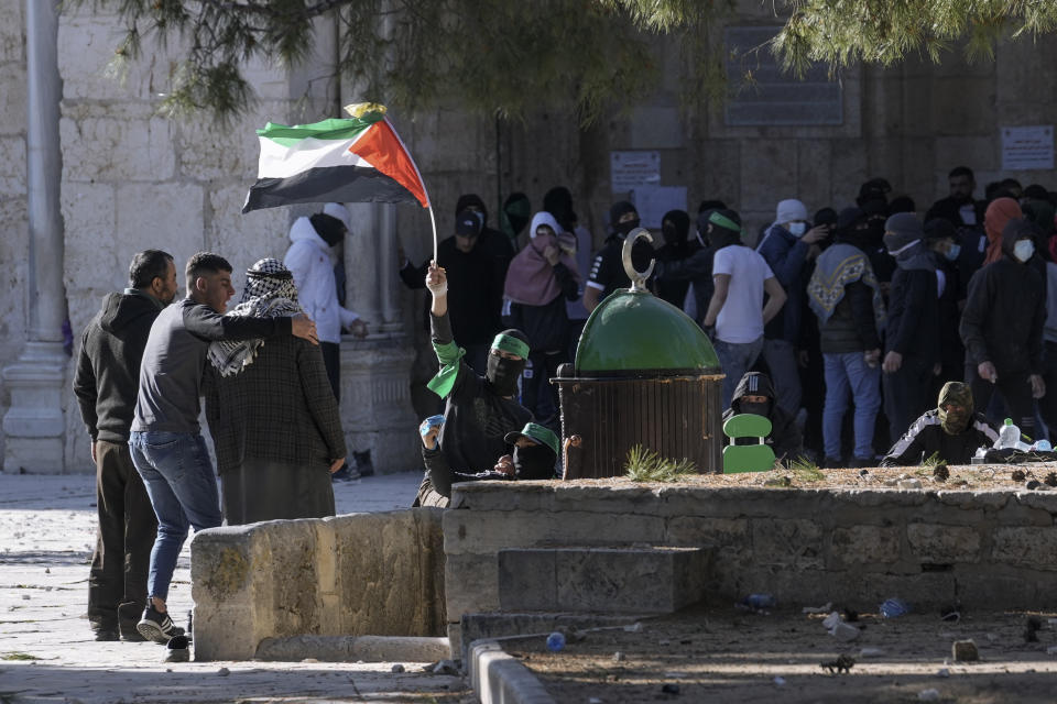 A Palestinian protester waves the Palestinian flag during clashes with Israeli security forces at the Al Aqsa Mosque compound in Jerusalem's Old City Friday, April 15, 2022. (AP Photo/Mahmoud Illean)