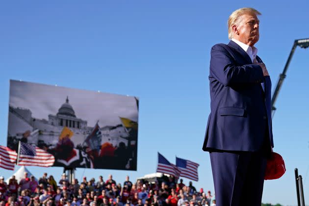 As footage from the Jan. 6, 2021, insurrection at the U.S. Capitol is displayed in the background, former President Donald Trump stands while a song, 