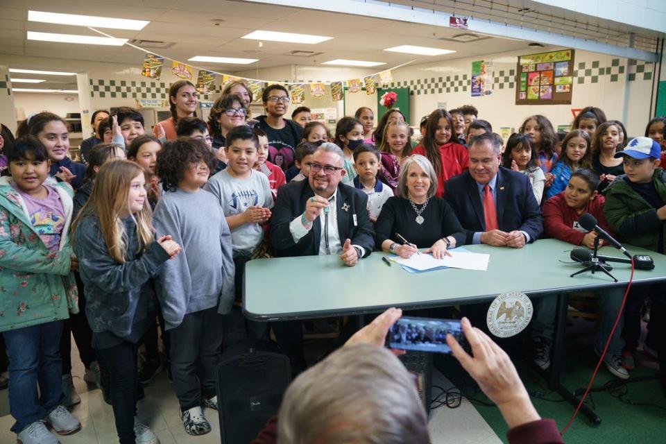 In this image provided by Gov. Michelle Lujan Grisham's office, the Democratic governor, center, signs a bill during a celebration with sponsors Sens. Michael Padilla, right, and Leo Jaramillo, left, at Pinon Elementary School in Santa Fe, N.M., Monday, March 27, 2023. The legislation provides universal free school meals for New Mexico students.