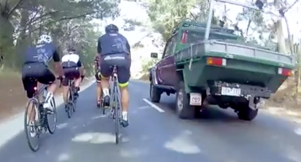 A pack of cyclists are riding on a road as a ute overtakes them in Victoria. 